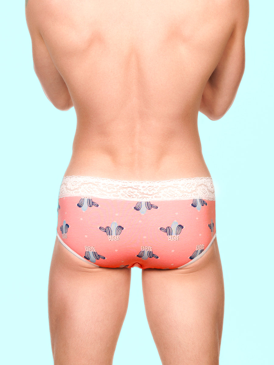 Back view of a man wearing pink XDress panties with white lace trim and cactus pattern against a blue background