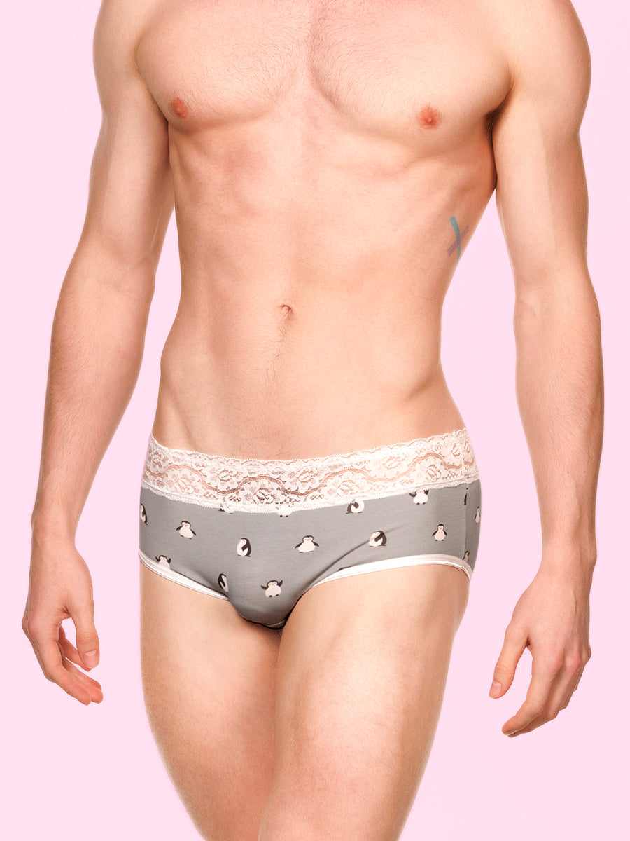 Front view of a man wearing pink XDress panties with white lace trim against a blue background
