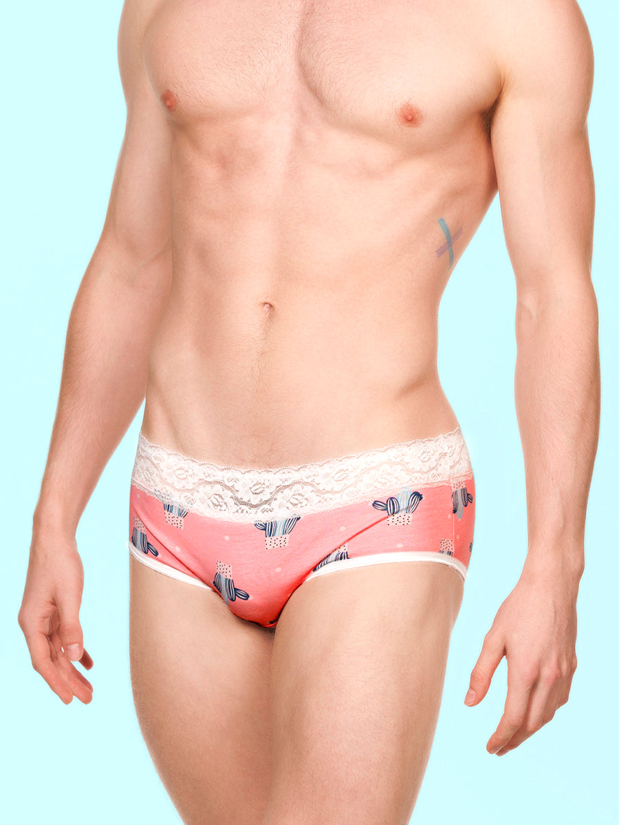 Front view of a man wearing pink XDress panties with white lace trim against a blue background