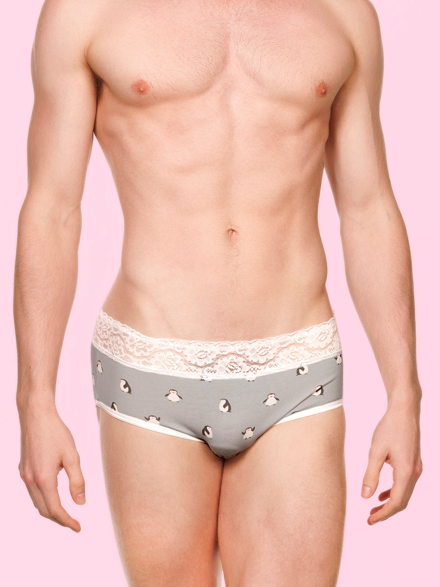 Front view of a man wearing pink XDress panties with white lace trim against a blue background
