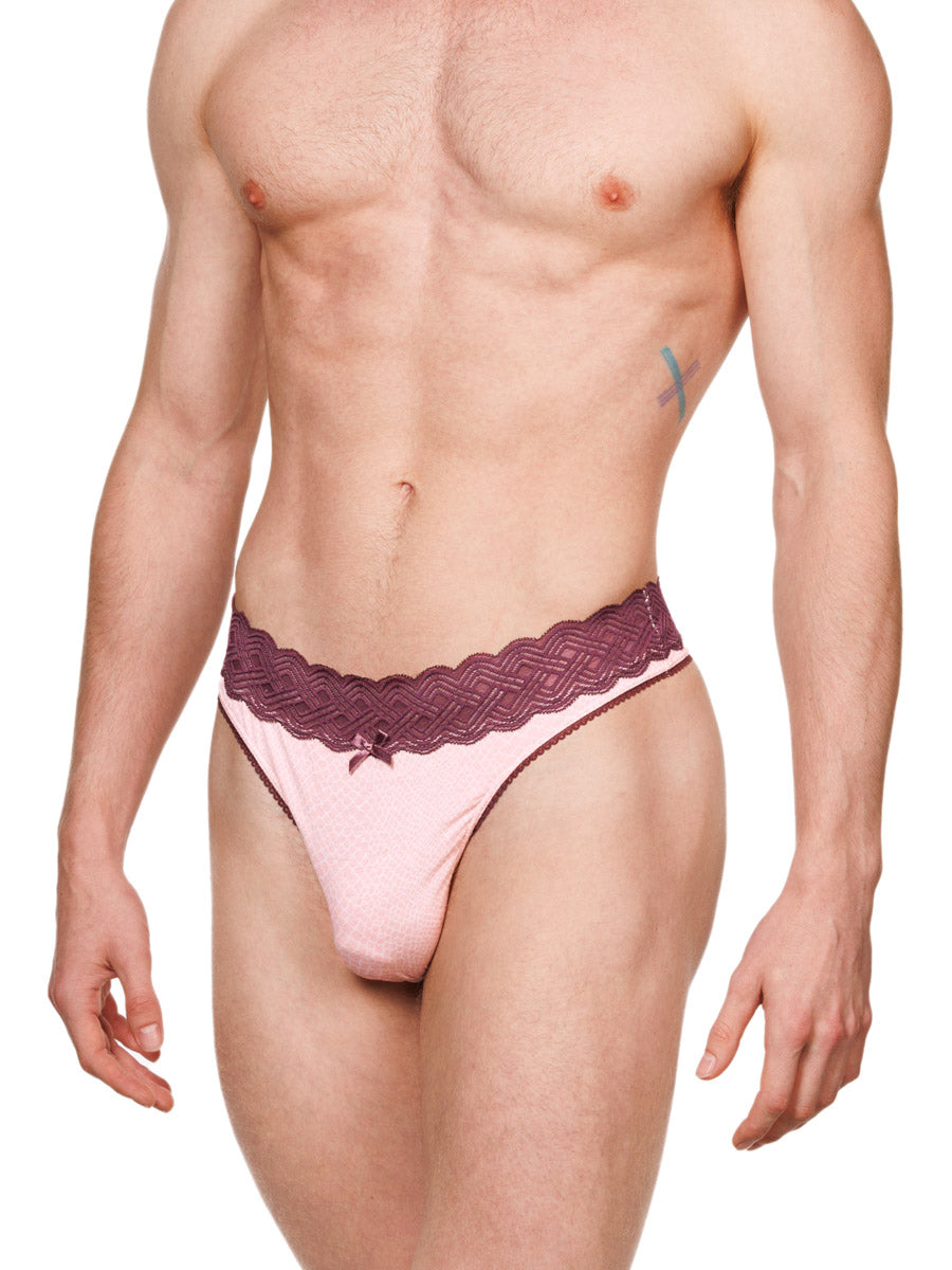 Side view of a male model wearing a pink XDress cotton thong with a red lace waistband