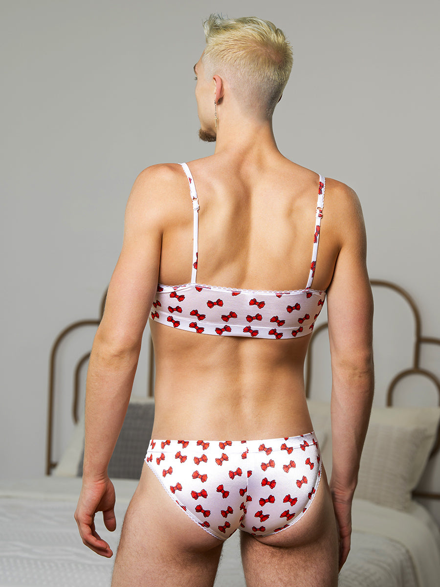 Rear view of a man wearing a matching white satin bra and panty set with red bow pattern.