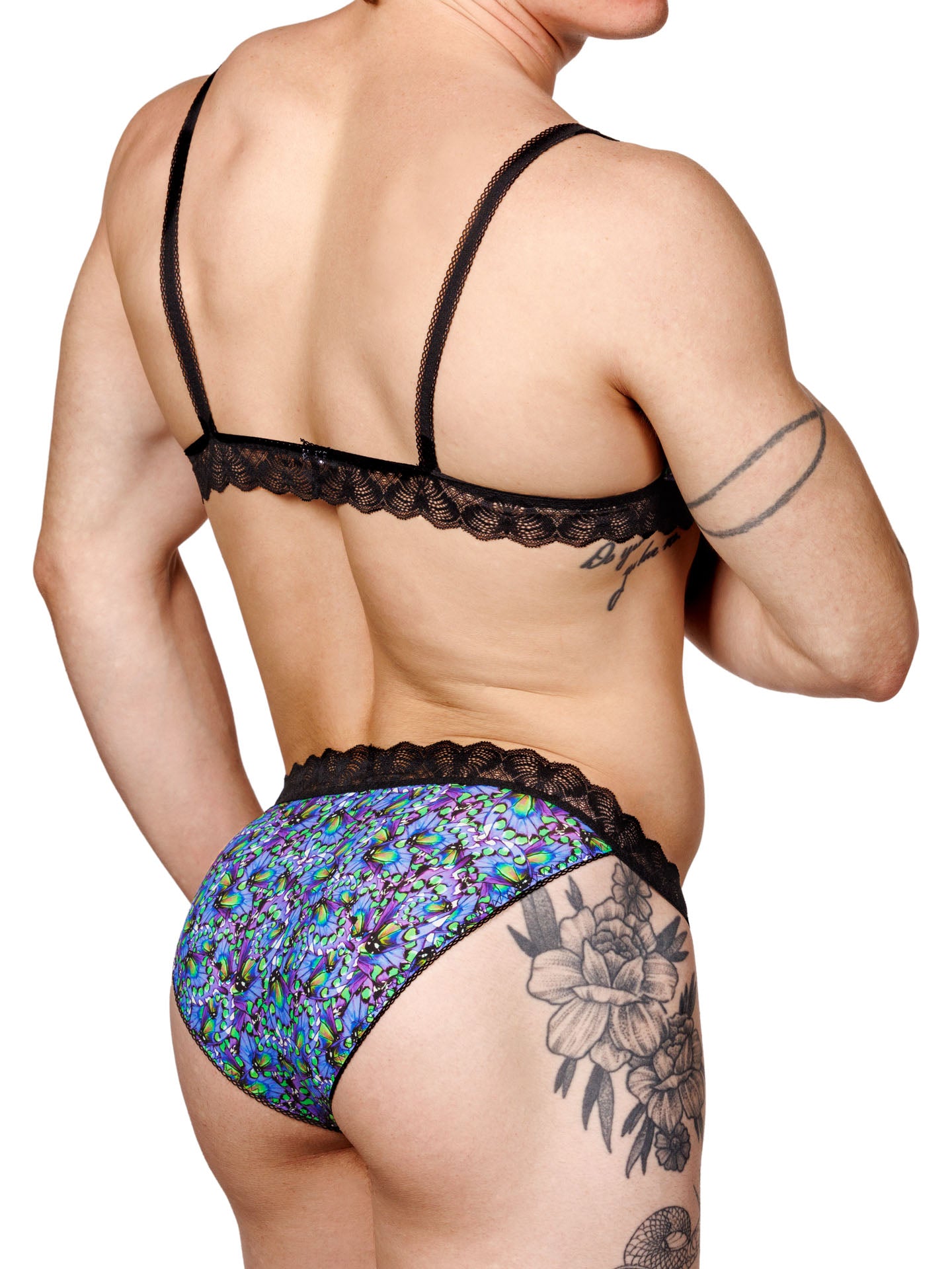 Male model wearing a blue floral print men's bralette with adjustable straps, lace trim, and a matching thong, shown from a back side angle.
