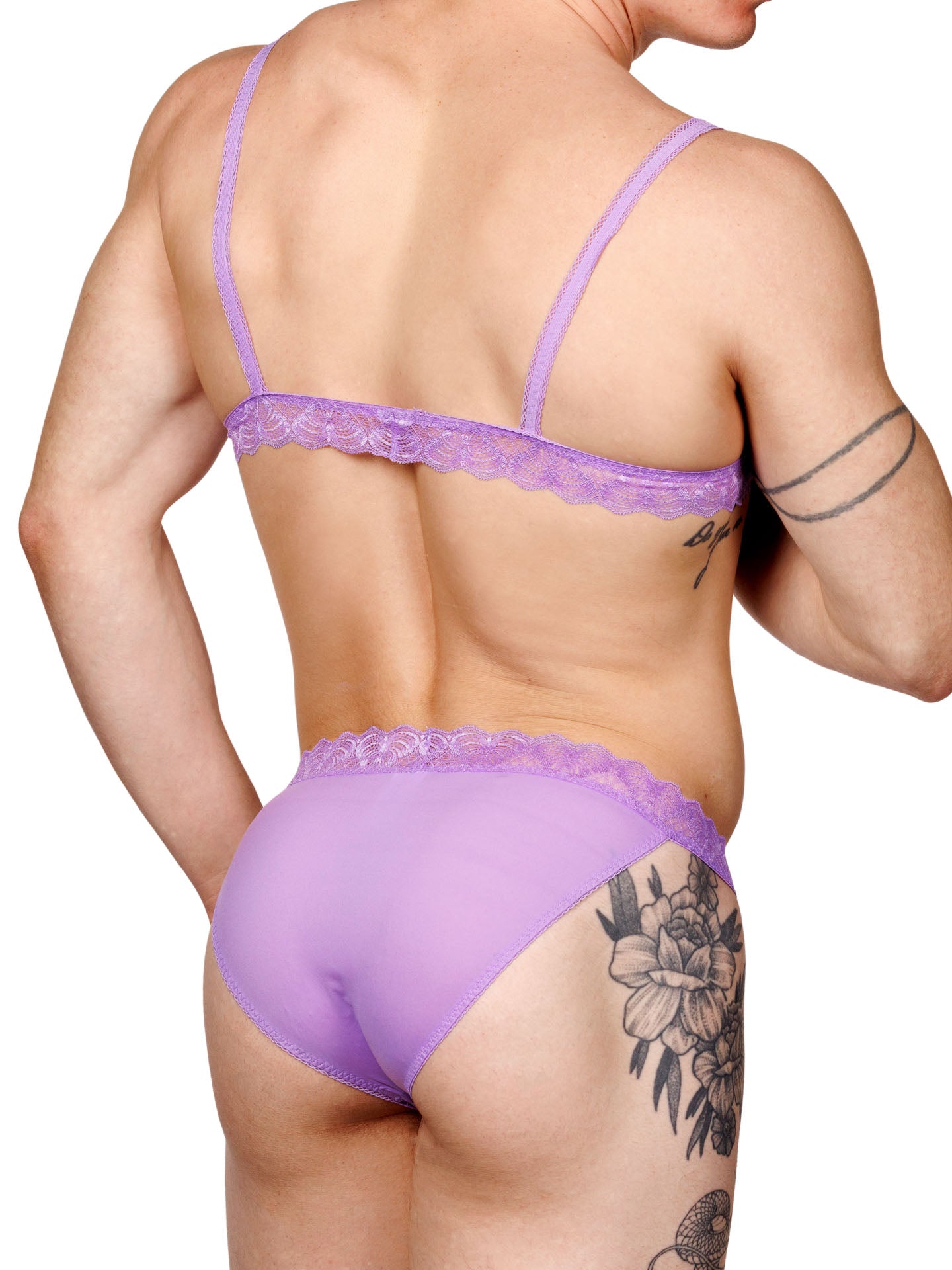 Male model wearing a purple lace-trim men's bralette with adjustable straps and a matching thong, shown from a back side angle.