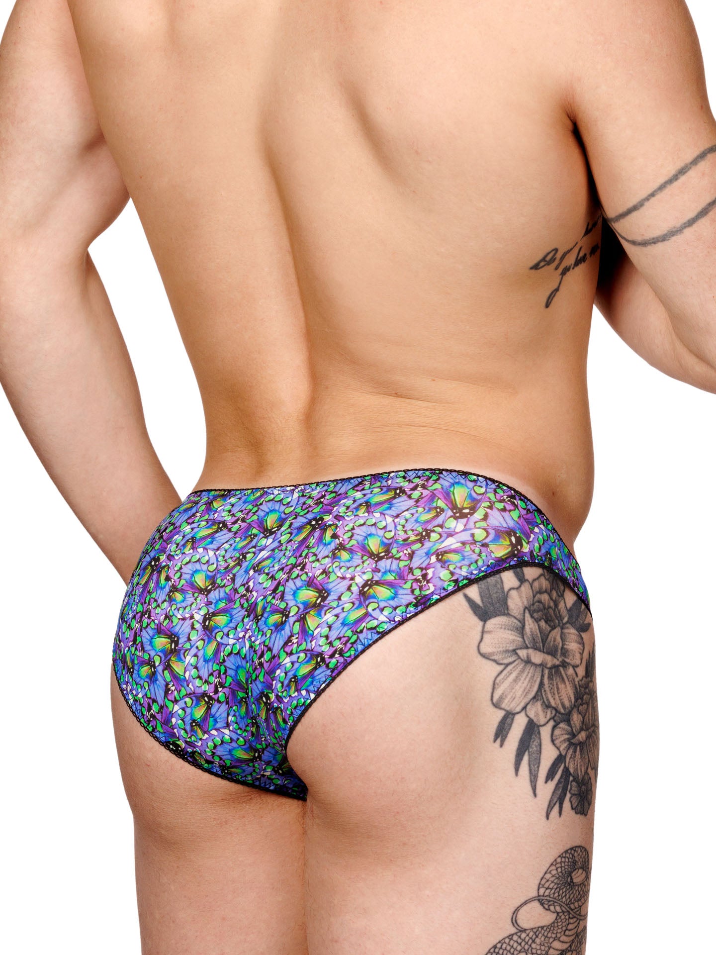Male model wearing a blue floral print men's panty with lace trim and a metallic charm at the front, shown from the back side.