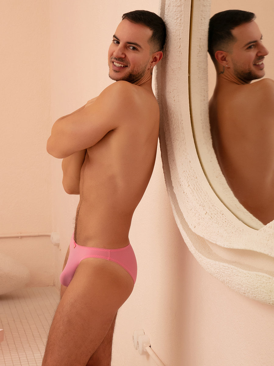 Side view of a man wearing pink XDress panties with matching bow. standing next to a mirror.