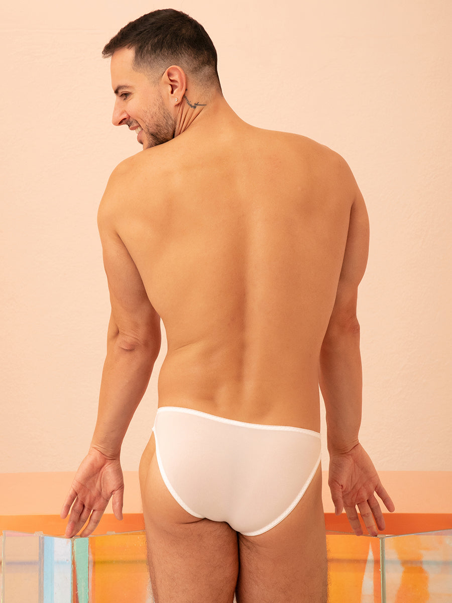 Rear view of a man wearing white XDress panties with a pink bow, leaning against a counter.