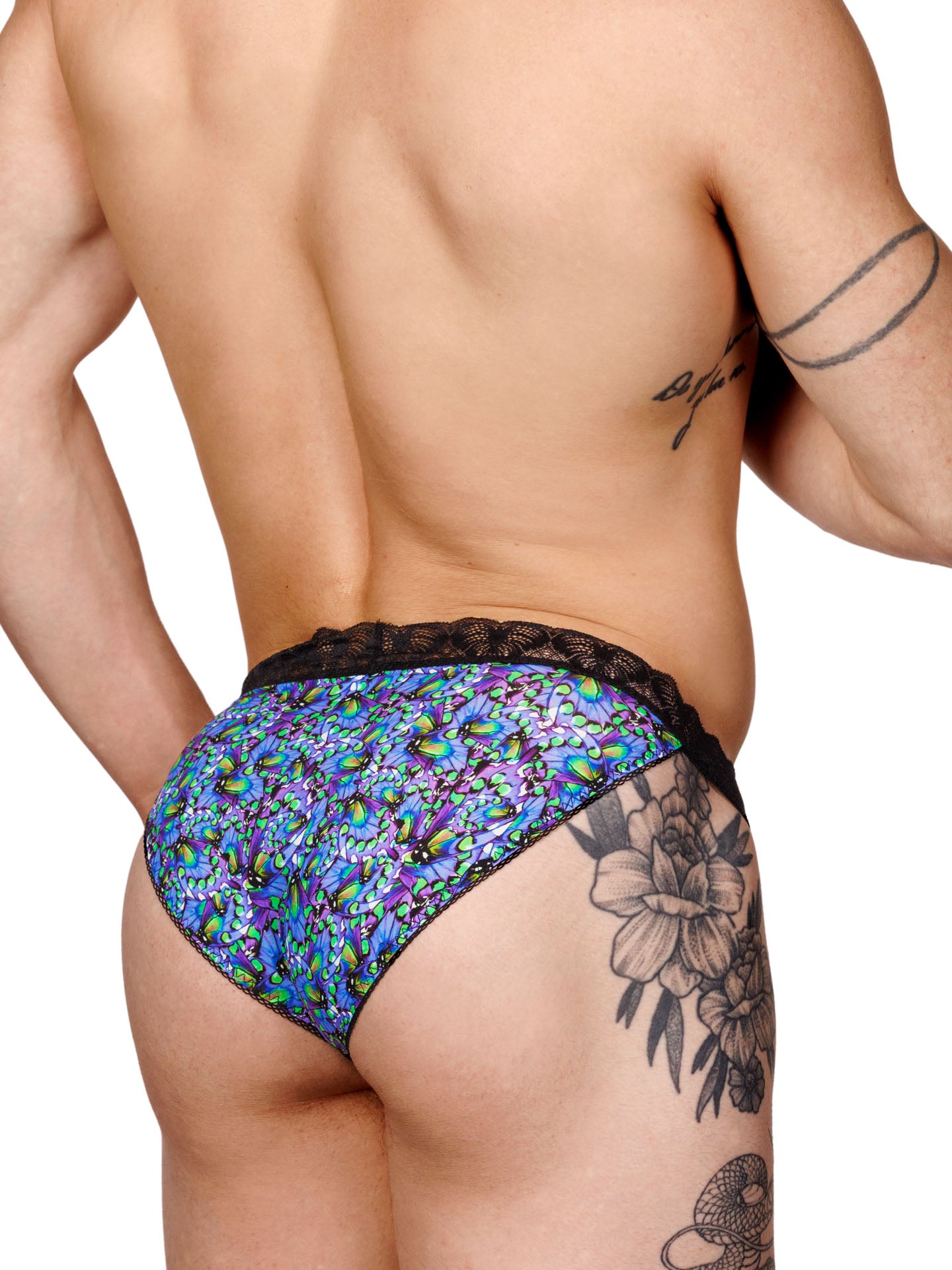 Male model wearing a blue floral print men's bikini panty with a black lace waistband and metallic charm at the front, shown from the back side.