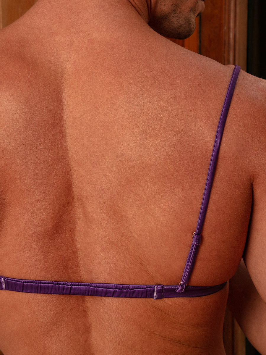 Closeup rear view of a man wearing a purple satin bra.