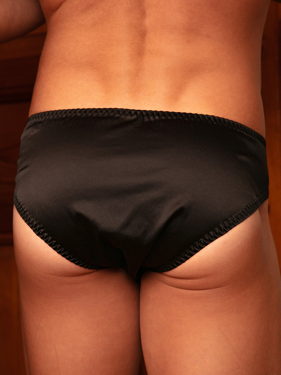 Closeup rear view of a man wearing black satin underwear with matching bows.