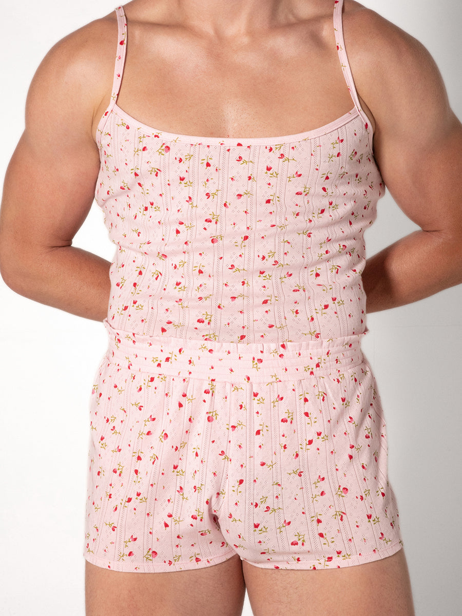 A man wearing a pink camisole with a red floral pattern and matching shorts
