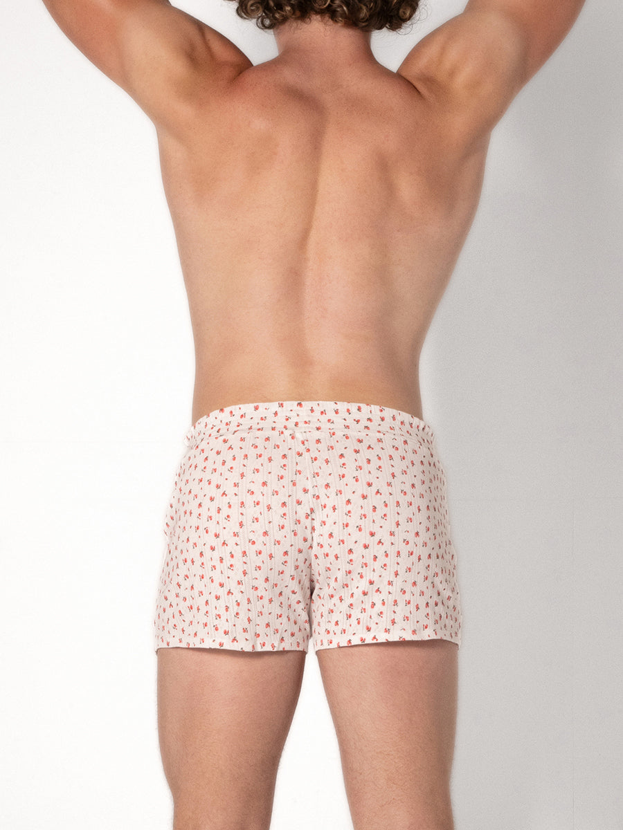 Man wearing white shorts with a red floral pattern on a plain background