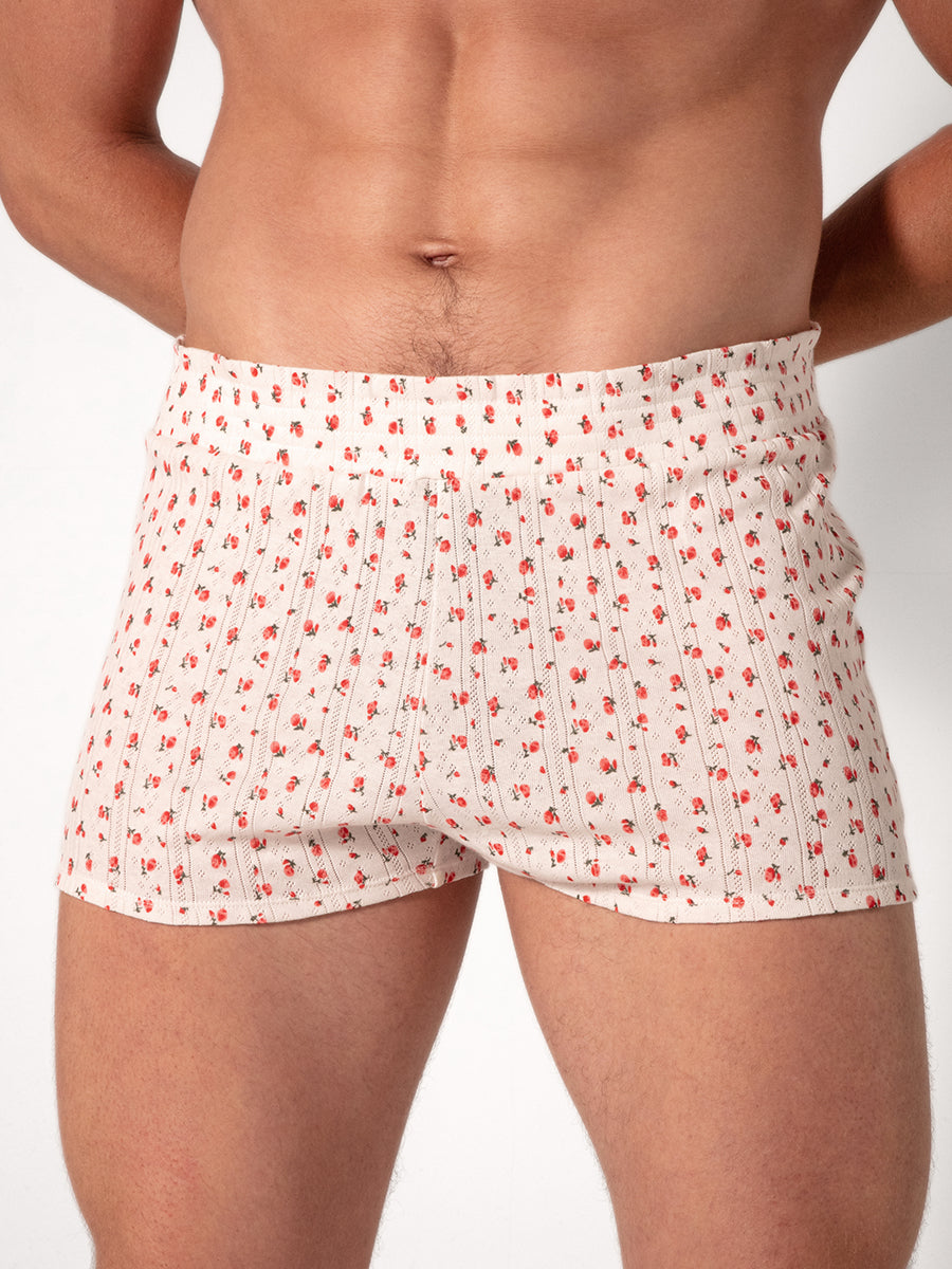Man wearing white shorts with a red floral pattern on a plain background