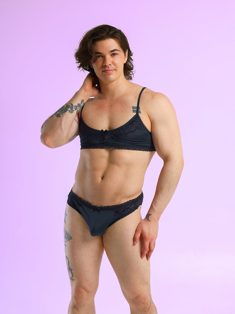 Front view of a man wearing a black bra and matching panties, against a purple background.