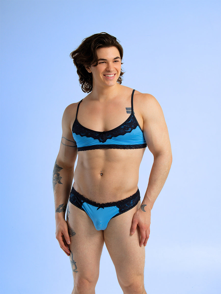 Front view of a man wearing a matching blue bra and panty set with black lace trim, against a blue background.