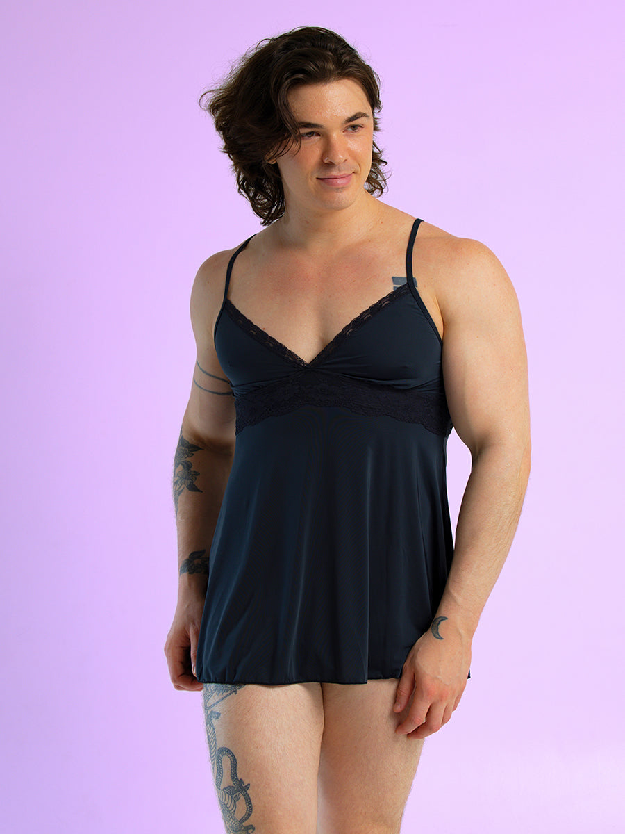 Front view of a man wearing a black babydoll with thin shoulder straps, against a purple background.