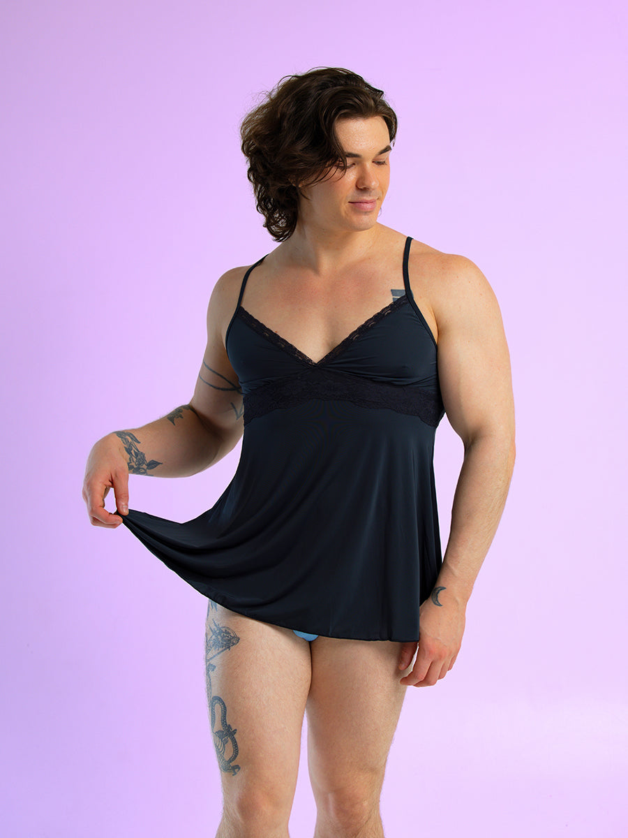 Front view of a man wearing a black babydoll with thin shoulder straps, against a purple background.