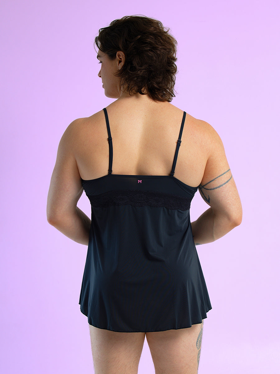 Back view of a man wearing a black babydoll with thin shoulder straps, against a purple background.