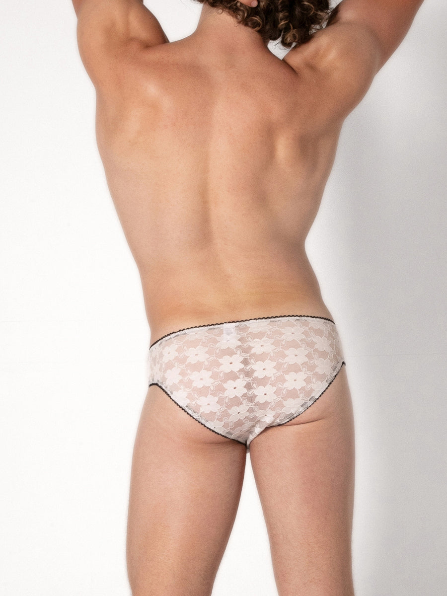 Rear view of a man wearing white lace underwear with black trim on a plain background